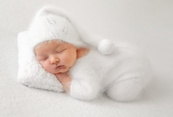 newborn-sleeps-quietly-fluffy-white-pillow-wearing-cozy-white-outfit-hat-with-hands-tucked.jpg